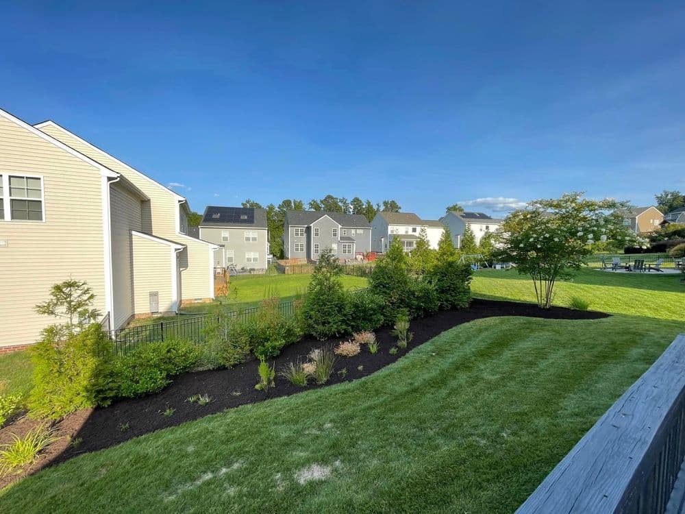 Residential backyard with manicured lawn and garden, surrounded by houses under a clear sky.