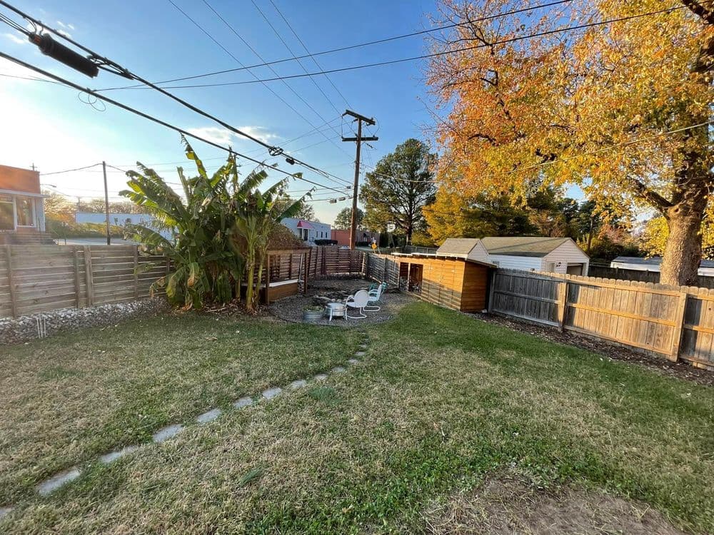 Backyard with seating area, trees, and wooden sheds under a clear sky.