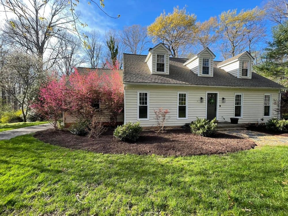 Charming white house with landscaped yard and vibrant pink flowers under a clear blue sky.