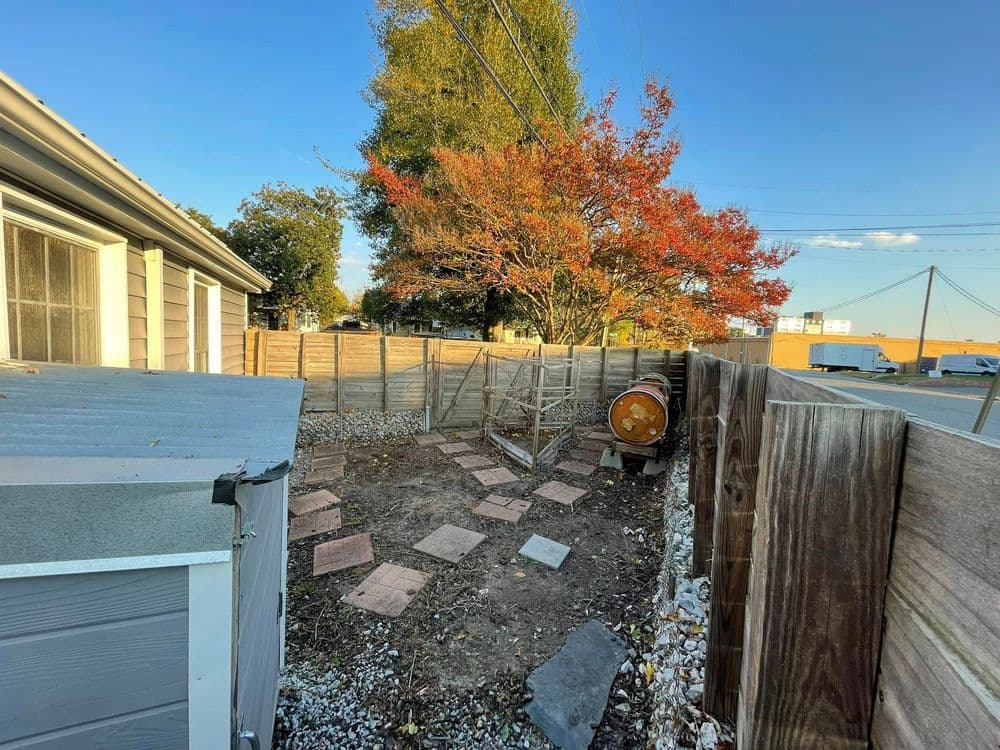 Backyard area with wooden fence, paving stones, and a tree showing autumn colors.